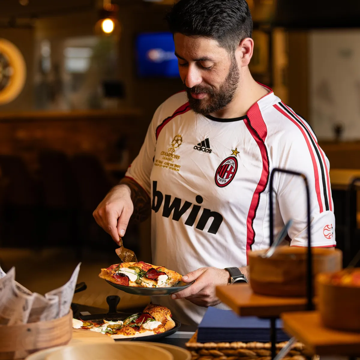 Ein Mann im Fußballtrikot bereitet eine Pizza in einem Restaurant zu.