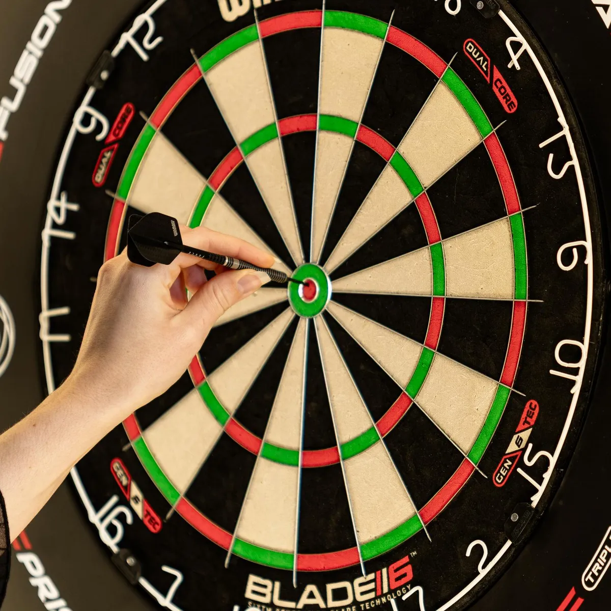 Eine Hand wirft eine Dartpfeil auf die Mitte einer Dartscheibe.