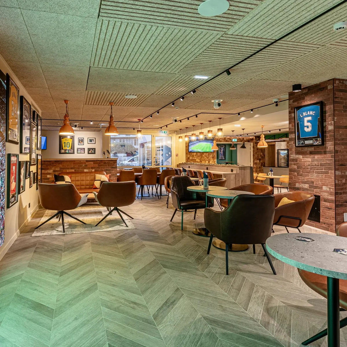 Un espace intérieur avec des sièges, des tables et un grand écran affichant un terrain de football, entouré de décorations sportives