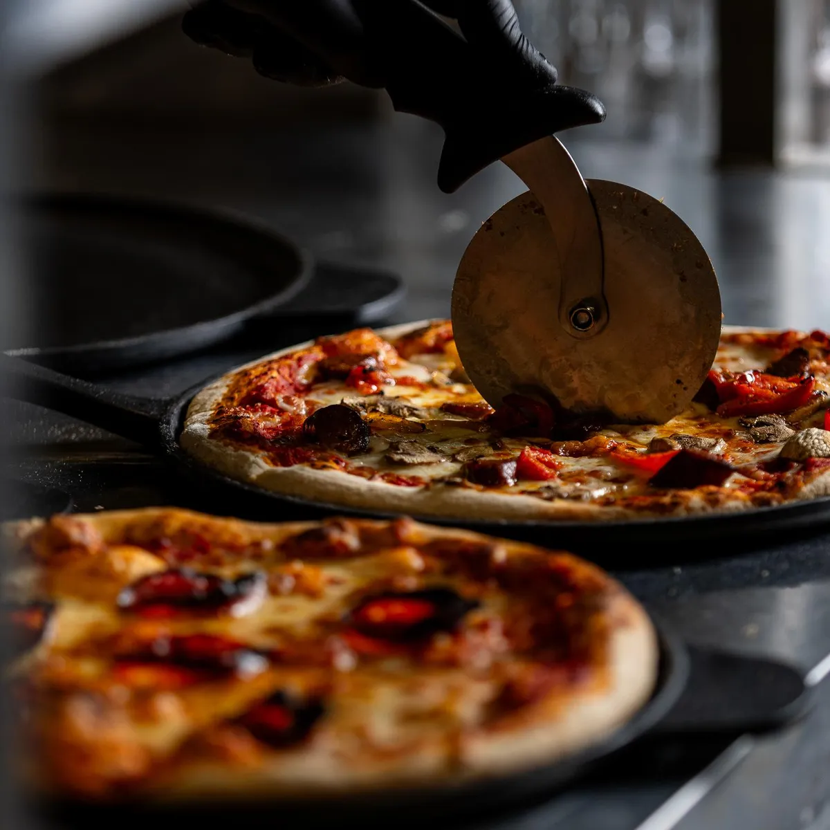 Eine Pizza wird mit einem Pizzarad auf einem Backblech geschnitten.