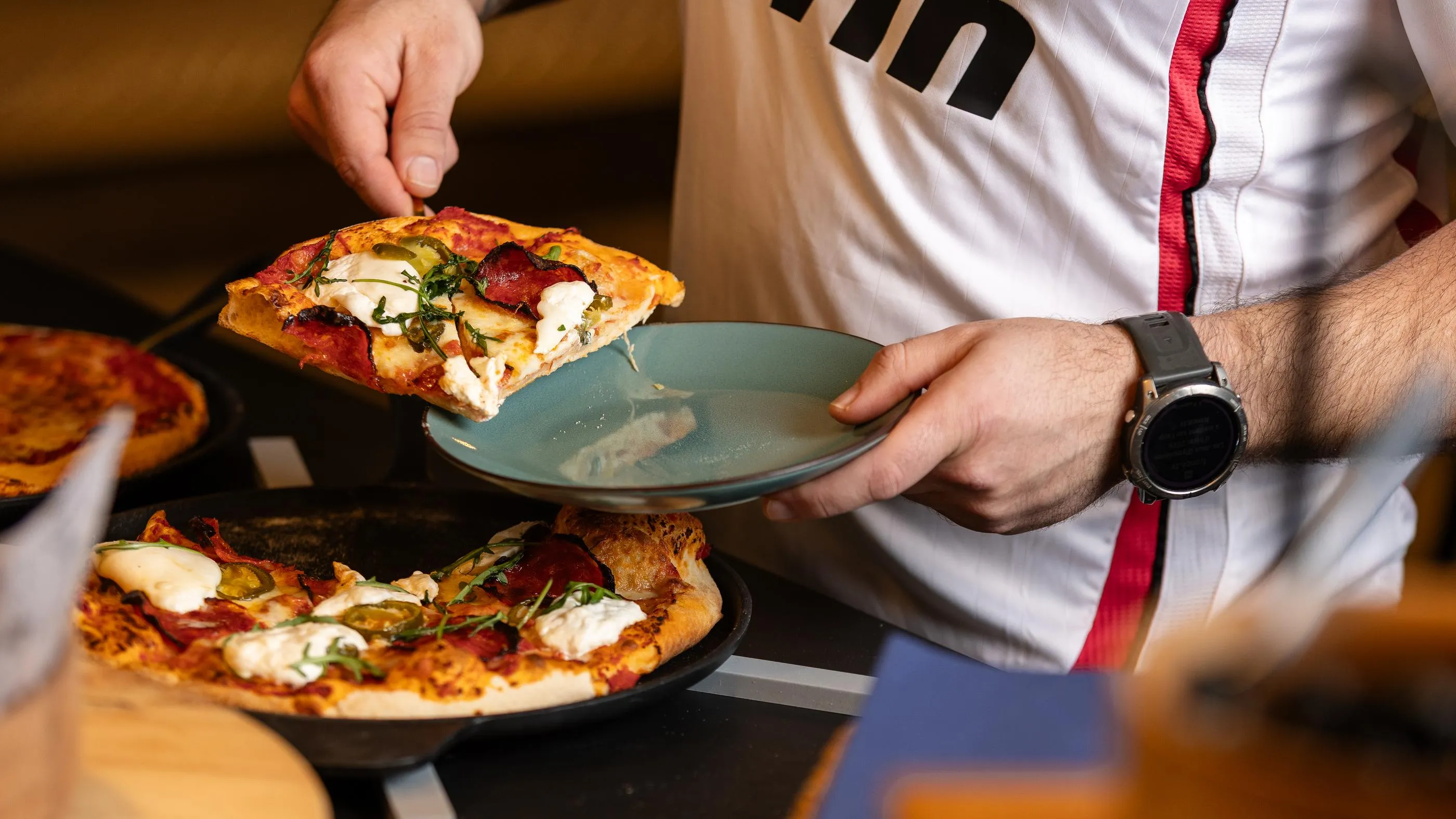 Une personne en tenue de chef sert une part de pizza sur une assiette verte