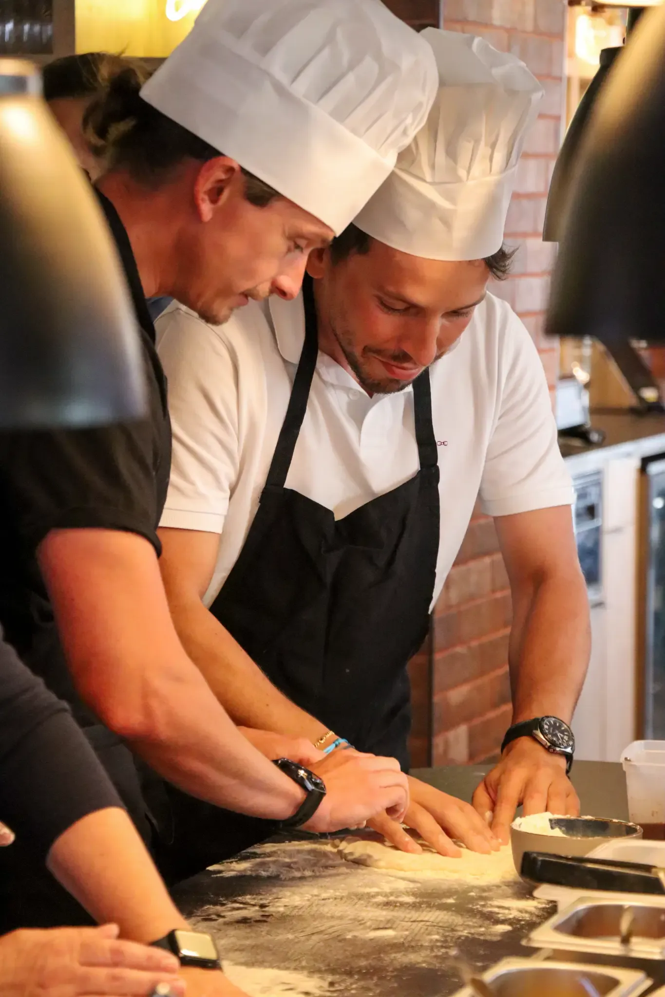 Zwei Personen mit Kochmützen und Schürzen kochen gemeinsam in einer Profiküche.