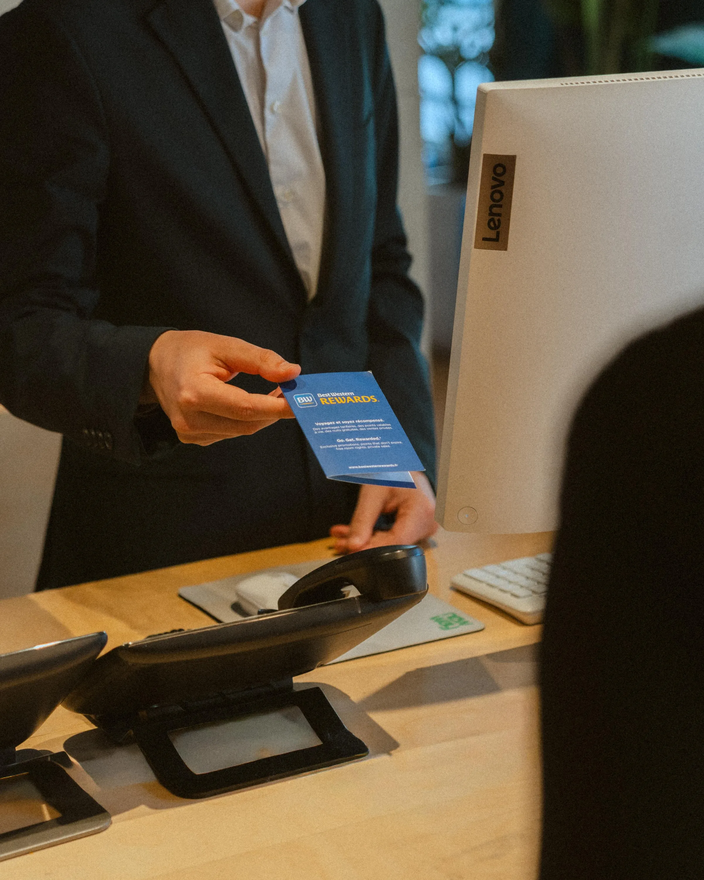 Eine Person reicht einem Mitarbeiter vor einem Lenovo-Laptop eine Best Western Rewards-Karte.