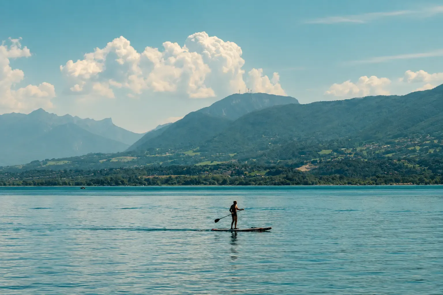 A person is paddleboarding on a lake with mountains in the background.