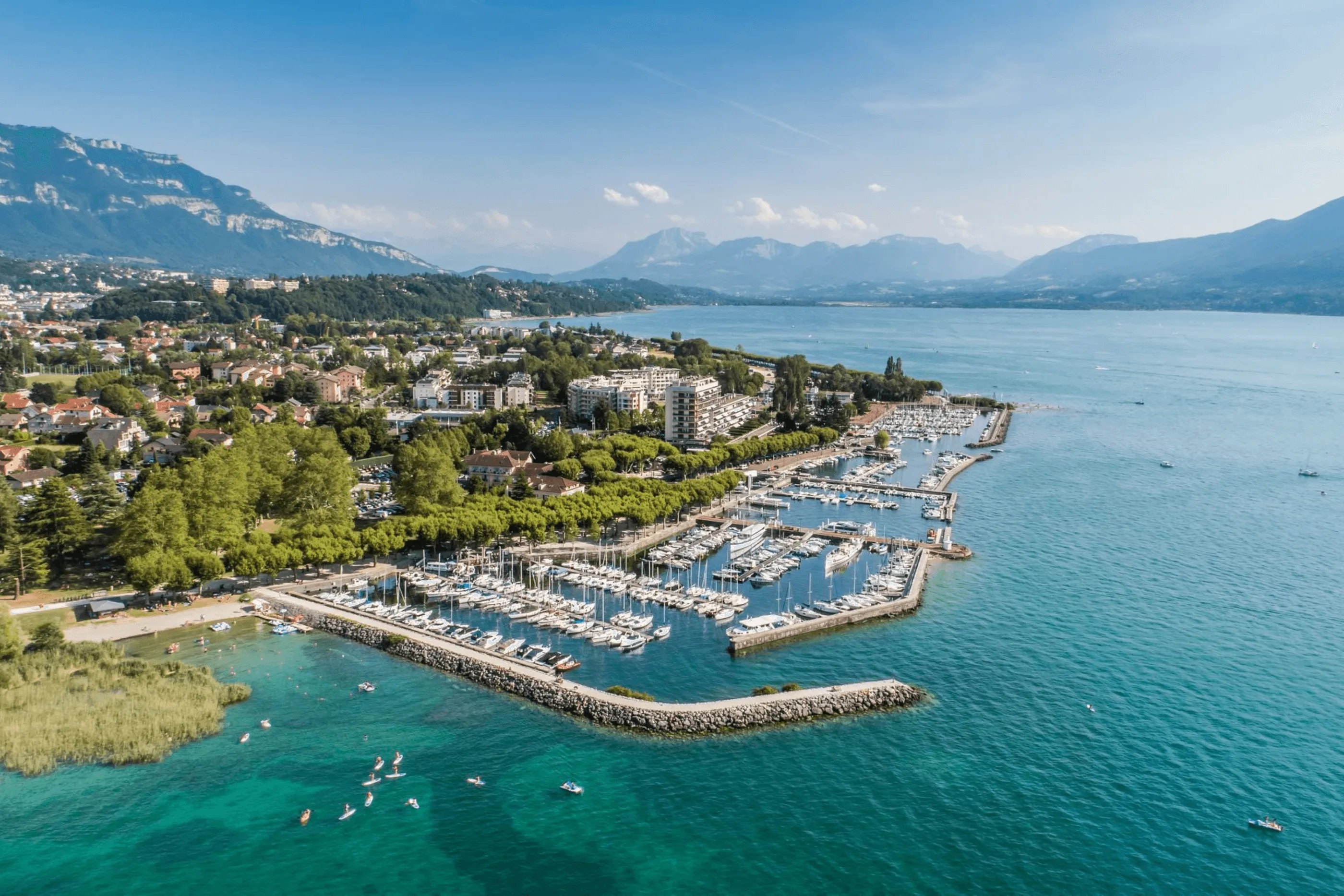 Village by a lake with marina, mountains in the background, and people paddleboarding in the water.